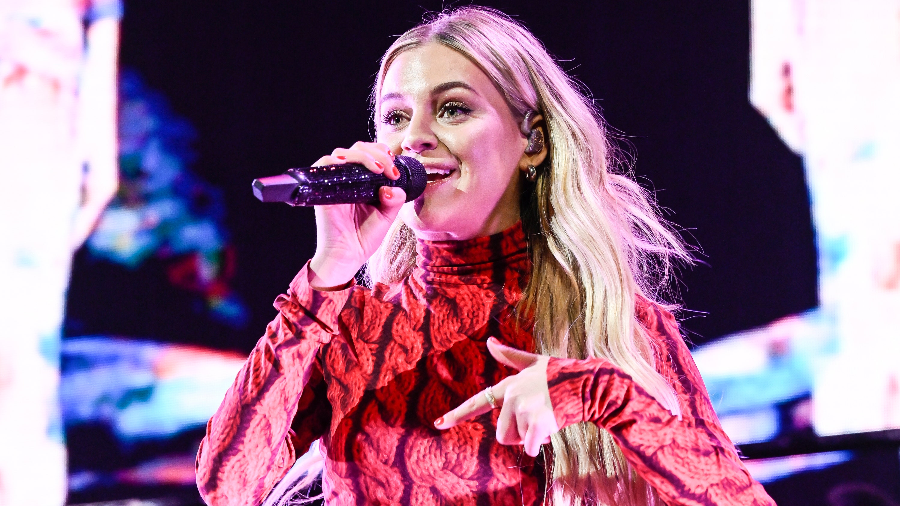 Kelsea Ballerini in a red patterned top singing into the microphone